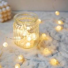 a mason jar filled with fairy lights sitting on top of a white table covered in snow