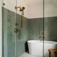 a white bath tub sitting in a bathroom next to a walk in shower and wooden stool