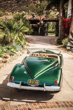 an old green car parked in front of a palm tree lined driveway with trees and bushes