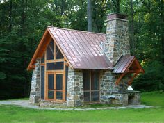 a small stone building with a metal roof and chimney in the middle of a grassy area