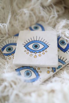 two ceramic coasters with blue eyes on them sitting on a white fur covered surface