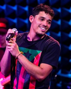 a young man holding a microphone in his right hand and smiling at the camera while standing on stage