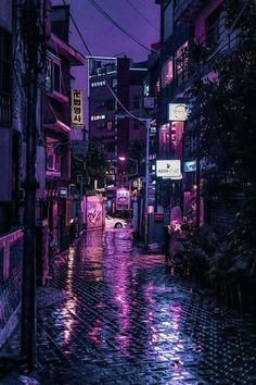 a city street at night with rain on the ground and buildings lit up in purple