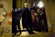 the joker and his friends are standing in front of a clock tower with their arms outstretched