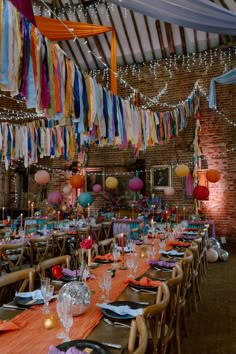 This image shows a dining area at a colourful barn wedding. This image shows rows of dining tables, with bright orange table runners, tableware, orange and white napkins, brass candlesticks, candle holders and disco balls. Above the tables are strings of colourful streamers and round paper lanterns. Firehall Wedding Reception, Wedding Streamers, Festival Wedding Ideas, Village Hall Wedding, Funky Wedding, Wedding Dining, Wedding Setup, Dinner Setting, Female Jacket