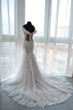 the back of a wedding dress on display in front of a window with sheer curtains