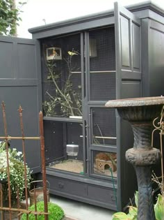 an outdoor area with a bird cage and water fountain in the center, surrounded by plants