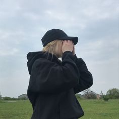 a woman in a black coat and hat is talking on her cell phone while standing in a field