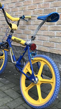 a blue and yellow bike parked next to a brick wall