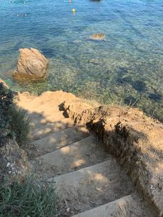 steps lead down to the water at a beach with boats in the distance and people swimming