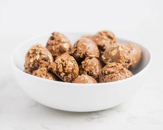 a white bowl filled with chocolate peanut butter balls on top of a marble countertop