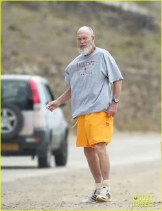 an older man in yellow shorts and a gray shirt is walking down the street with his dog