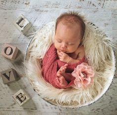 a baby is laying down in a bowl with blocks and flowers on the floor next to it