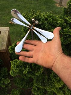 a hand holding four spoons in front of some bushes