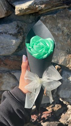 a person holding up a black paper box with a green rose in it and a white bow