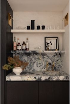 a kitchen with marble counter tops and black cabinetry, gold faucet handles