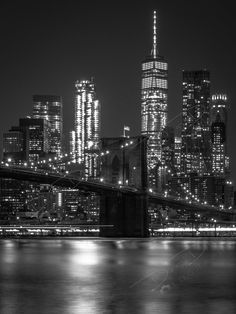 black and white photograph of the brooklyn bridge at night with city lights in the background