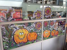 a store window with painted pumpkins and flowers on the glass, behind which there is a woman standing in front of it