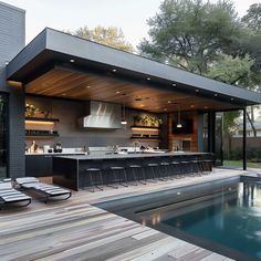 an outdoor kitchen next to a pool in the middle of a yard with lounge chairs