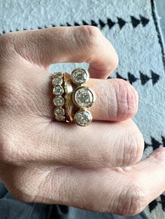 a person's hand holding a gold ring with three stones on it and two diamonds in the middle