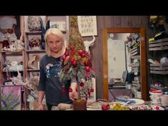 a woman standing next to a christmas tree in a room filled with shelves and other items