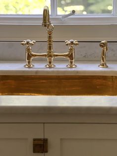 a kitchen sink with gold faucets in front of a window