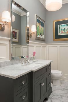 a bathroom with marble counter tops and gray cabinets, along with framed pictures on the wall