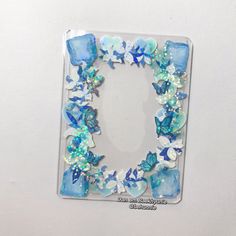 a clear square frame with blue and white glass flowers, butterflies and pearls on it