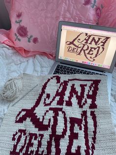 a laptop computer sitting on top of a bed next to a crocheted afghan