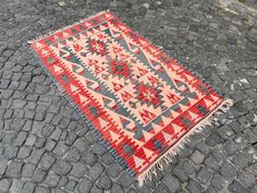 a red and blue rug sitting on top of a cobblestone road