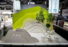 an exhibit booth with green and white designs on the wall, trees in vases