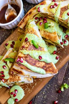 a wooden cutting board topped with quesadillas covered in guacamole and pomegranate