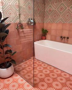 a bath tub sitting next to a plant on top of a tiled floor in a bathroom