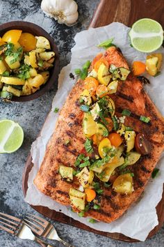 grilled salmon with vegetables on parchment paper next to fork and bowl of lemons