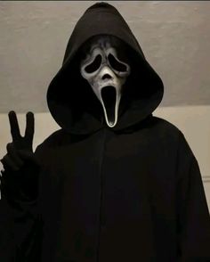 a person wearing a black hooded jacket with a white mask on their face and one hand in the air