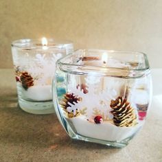 two clear glass candles with pine cones and snowflakes in them