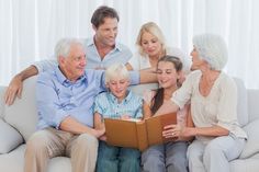 an older man sitting on a couch with two women and three children reading a book