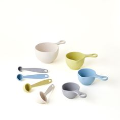 five different colored measuring cups and spoons on a white surface with one empty cup in the middle