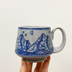 a hand holding a blue and white coffee cup with mountains on the outside, stars in the sky