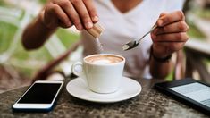 a person sitting at a table with a cup of coffee and spoon in their hand