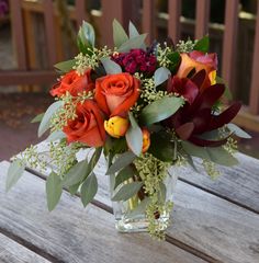 a glass vase filled with lots of flowers on top of a wooden table next to a bench