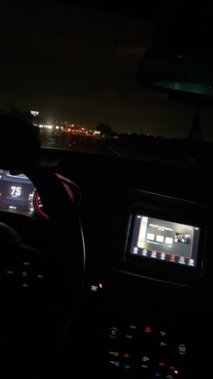 the interior of a car with dashboard lights on at night and city lights in the distance