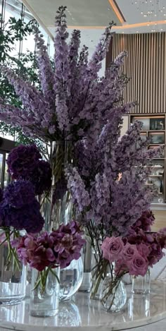 purple flowers in vases sitting on a table inside a building with glass walls behind them