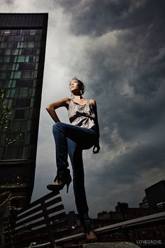 a woman standing on top of a metal rail next to a tall building under a cloudy sky