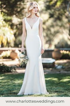 a woman in a white wedding dress is standing on the grass with her hands behind her back