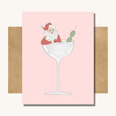 a card with a santa clause sitting on top of a wine glass and an olive in it