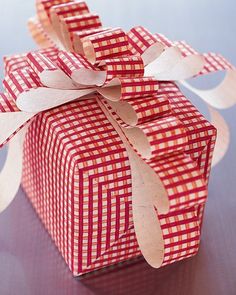 a red and white checkered gift box with ribbon on the top, sitting on a table