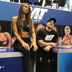 a woman sitting next to a man in front of a wall with pictures on it