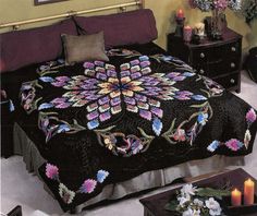 a bed with a black bedspread covered in flowers and purple pillows on top of it