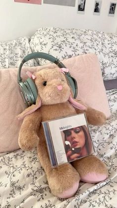 a teddy bear sitting on top of a bed next to headphones and a book